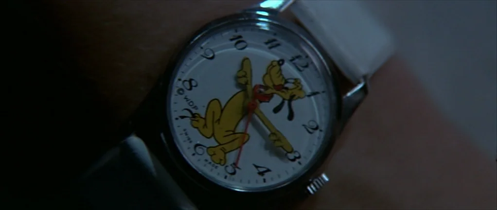 The Moon in the Gutter (1983) movie still: closeup — A close-up view of a wrist wearing a round analog watch. The white watch face features a…