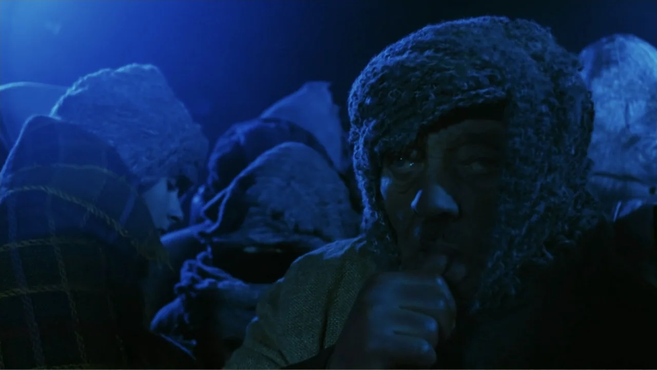O-Bi, O-Ba: The End of Civilization (1985) movie still: closeup — A dark, dimly lit indoor space is filled with people in heavy winter clothing. An…