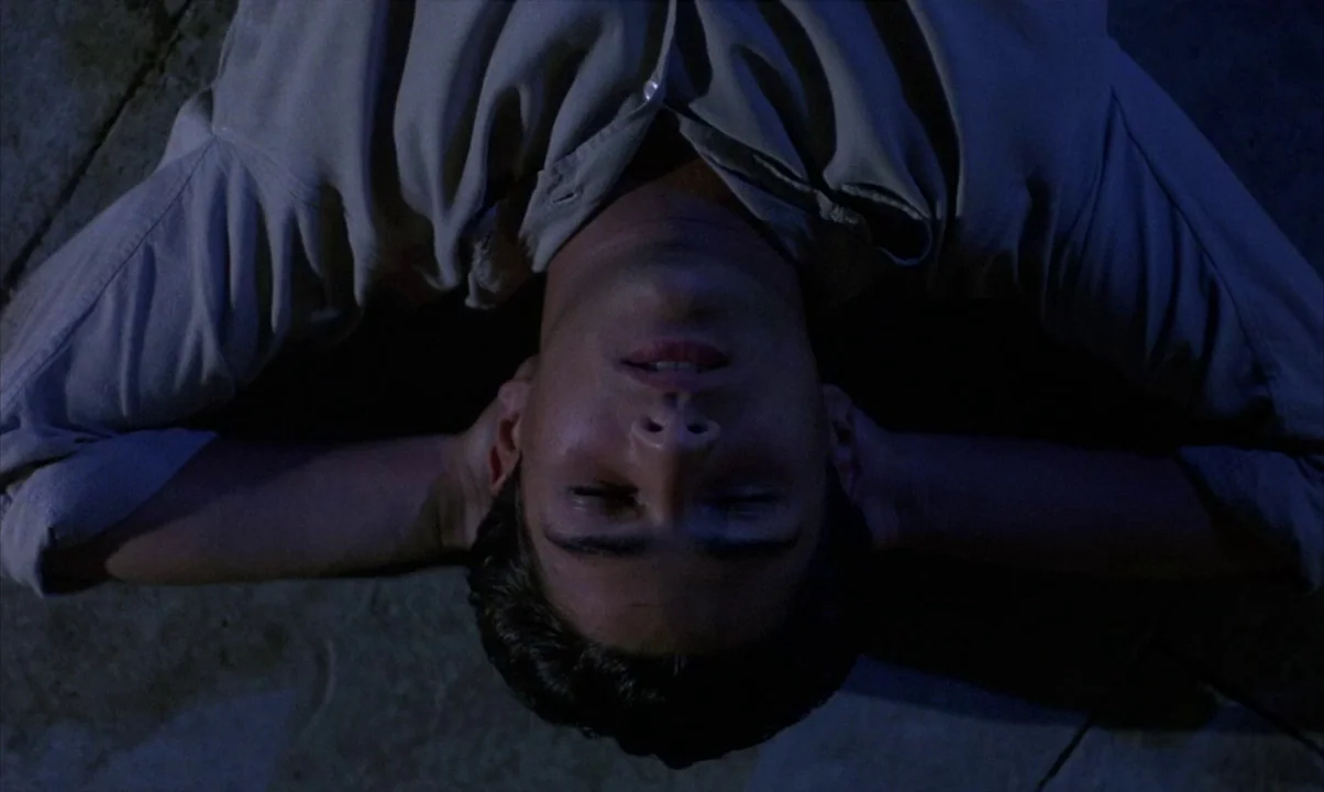 Cinema Paradiso (1988) movie still: closeup — The subject lies flat on a dark ground surface in low light. He is resting with his head back and…
