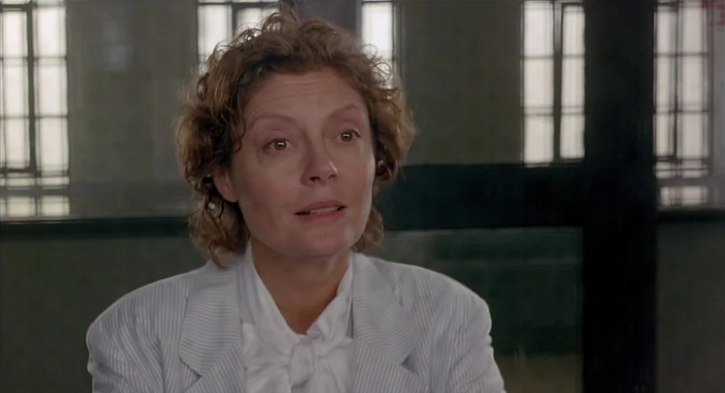 Dead Man Walking (1995) movie still: medium — An institutional room with green metal-framed windows separated by thick dividers. A middle-aged woman…
