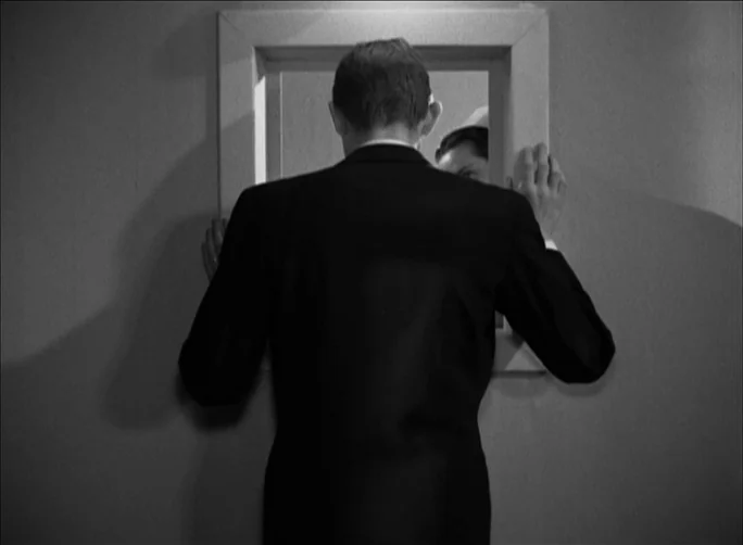 Summer with Monika (1953) movie still: medium — A plain interior wall features a small rectangular opening framed by thick molding. A man wearing a…