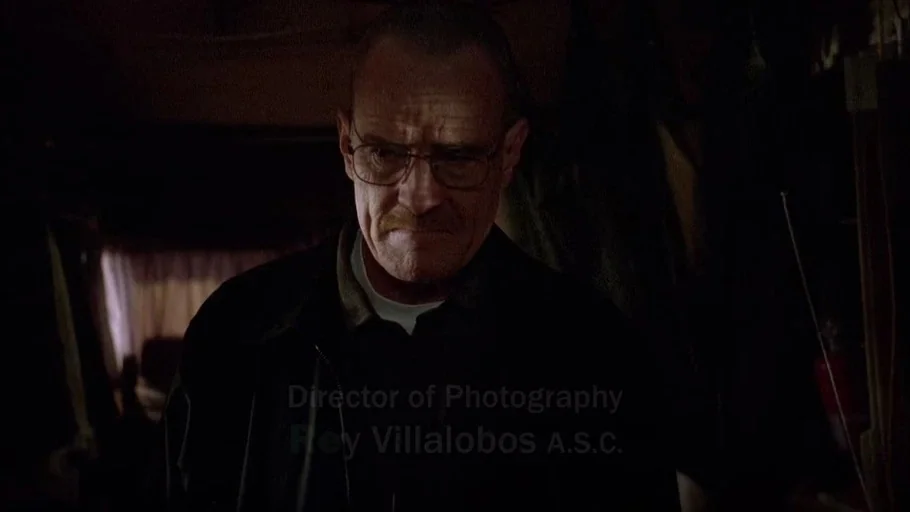 Breaking Bad (2008) movie still: medium — The interior of a cramped, dimly lit vehicle contains cluttered shelves and dark panels. A middle-aged man…