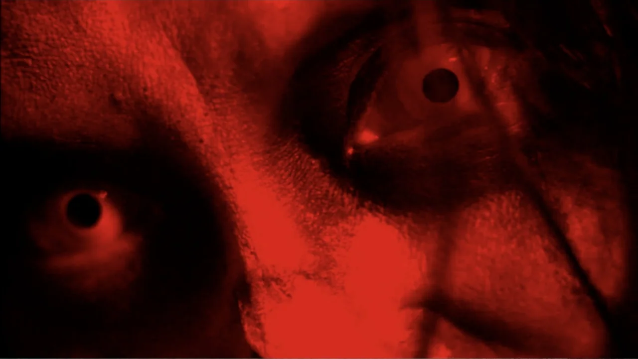 Abandoned Dead (2015) movie still: closeup — A dark space is lit entirely by an intense red light source. A person's face is positioned close to the…