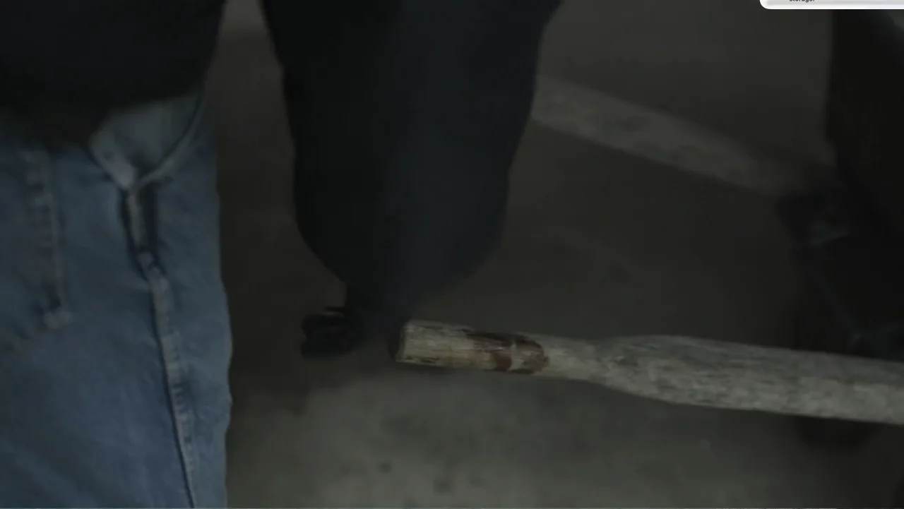 Murder at Carter County Mines (2023) movie still: medium — A dark indoor workroom contains a person and a wooden tool handle. The subject holds the…