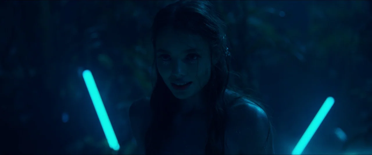 Birds of Paradise (2021) movie still: medium — A dark, blurred jungle setting at night is filled with shadows and foliage. A young woman with…