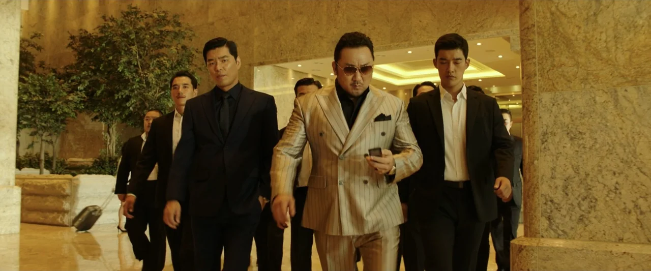 The Gangster, the Cop, the Devil (2019) movie still: fullbody — A spacious hotel lobby features polished marble walls and floors with indoor…