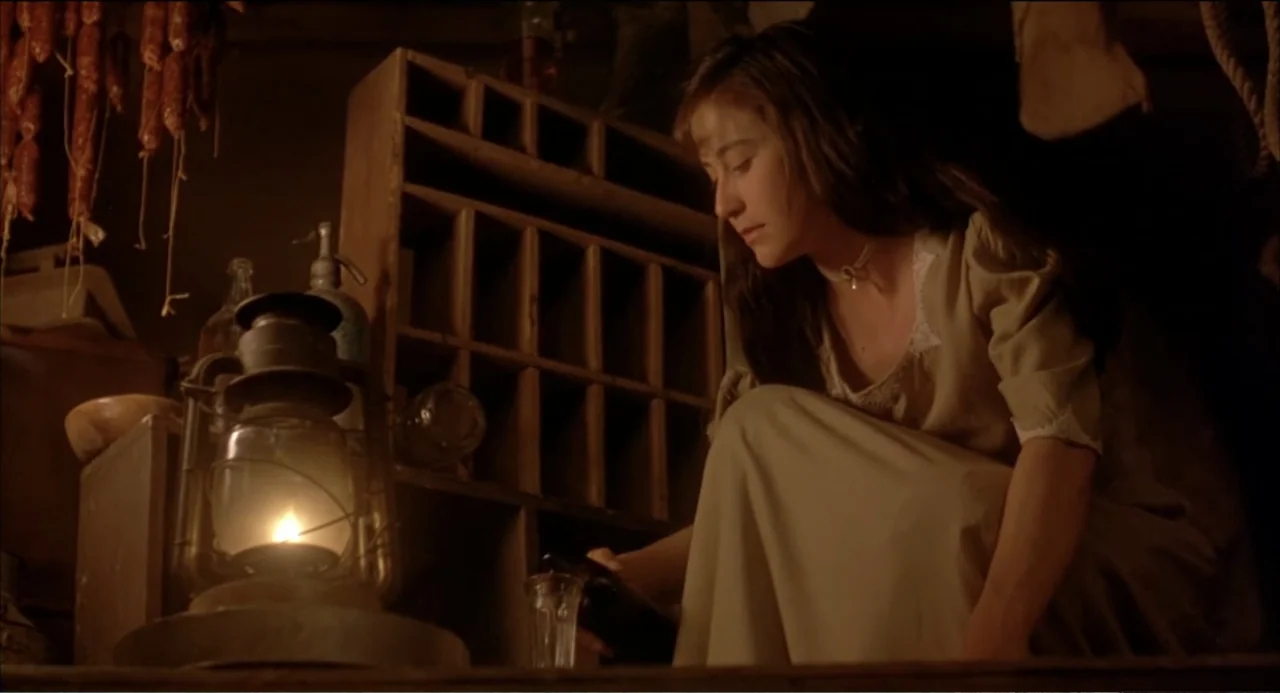 Like Water for Chocolate (1992) movie still: medium — A dimly lit wooden pantry contains storage shelving and hanging meat links. A young woman in a…