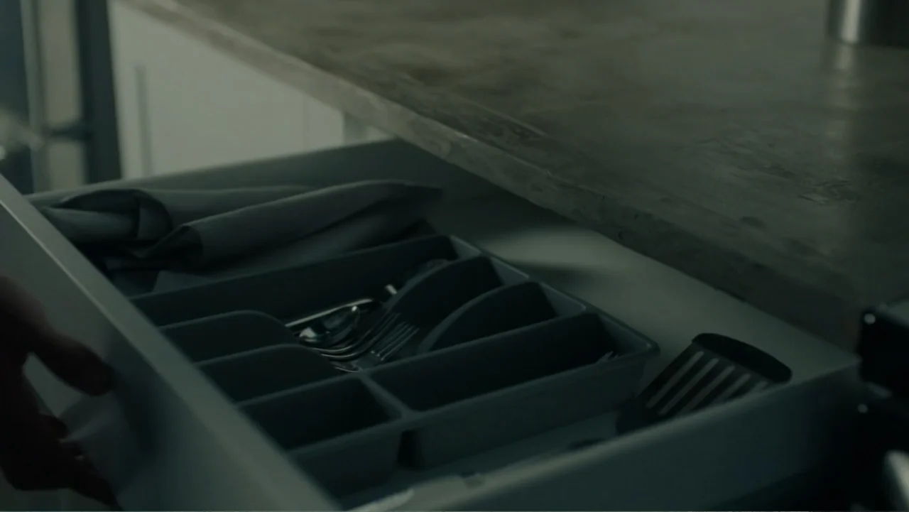 Sightless (2017) movie still: closeup — A dark gray kitchen drawer is pulled open to reveal organized cutlery compartments. Silverware rests inside…