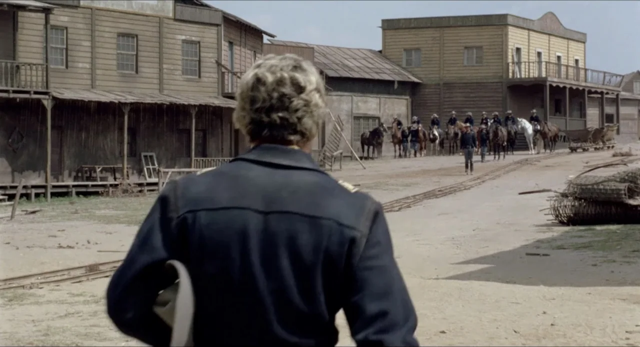 A Stranger in Town (1943) movie still: medium — A dusty western town street features wooden buildings with covered walkways and horsemen waiting.