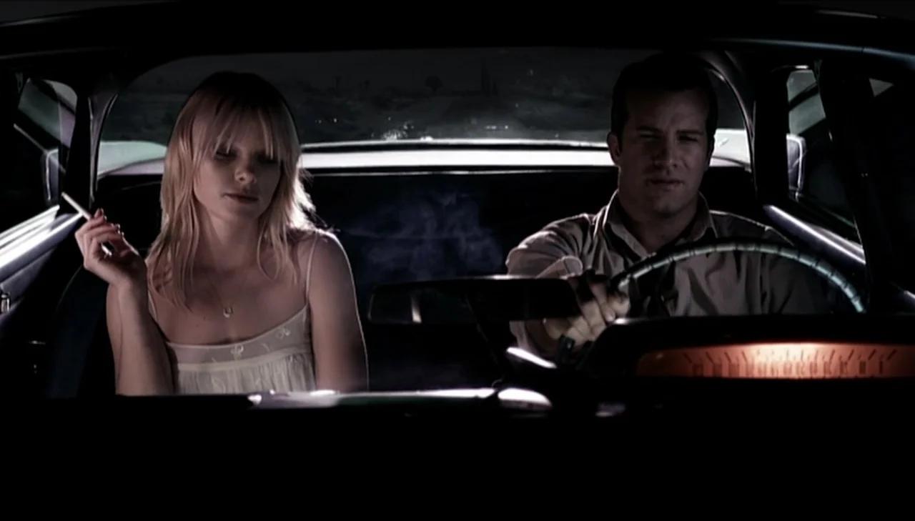 Dark Country (2009) movie still: medium — A dark vehicle cabin at night with a glowing amber dashboard instrument cluster. A man drives the car…