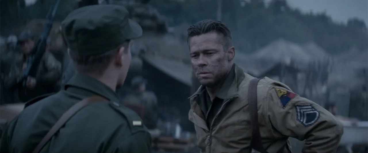 Fury (2014) movie still: medium — A military encampment with tents and equipment obscured in the soft focus background. An older soldier with a…