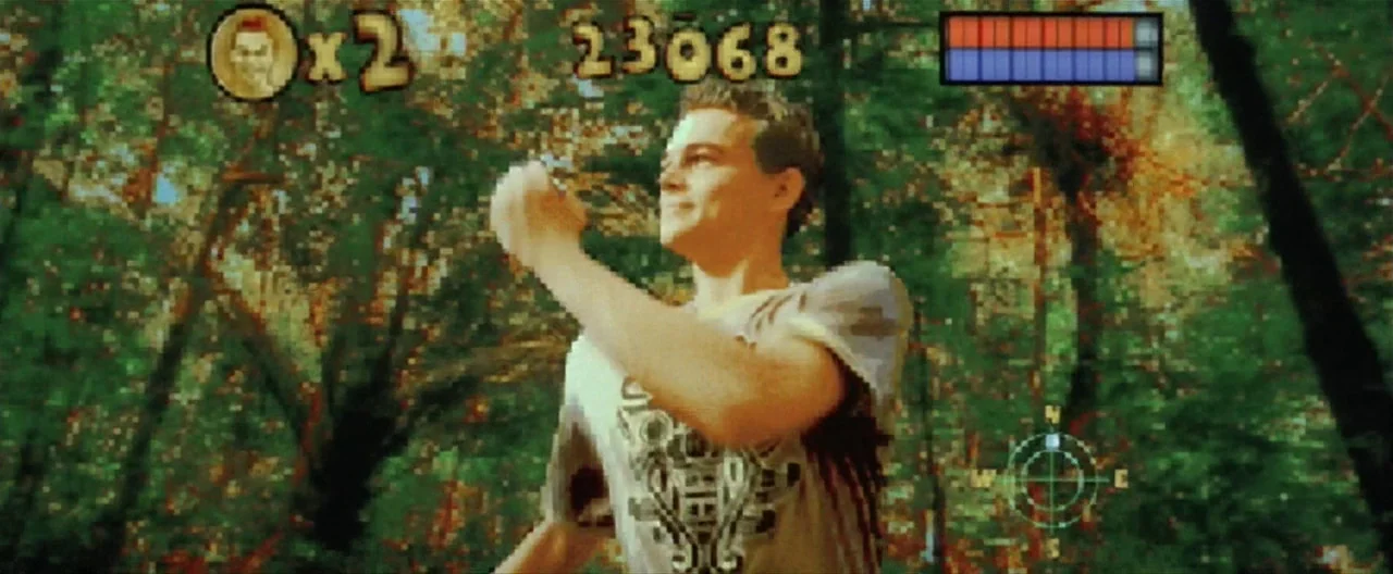 The Beach (2000) movie still: medium — A man walks through a dense woodland with sun-dappled green leaves and dark trunks. An overlaid video game…