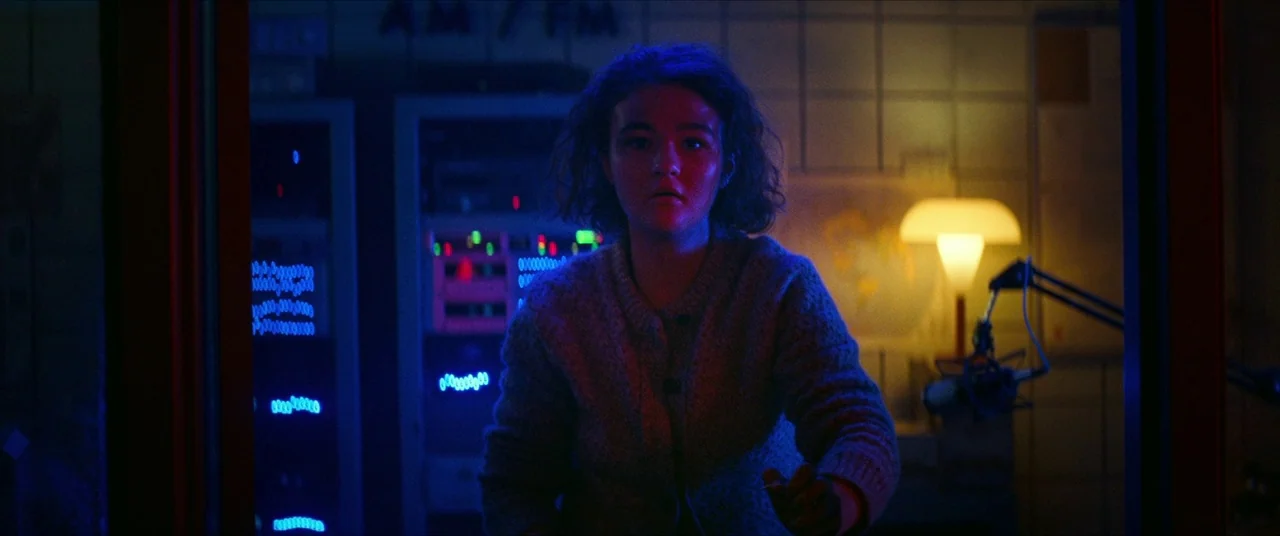 A Quiet Place Part II (2020) movie still: medium — A radio broadcast booth features blinking blue equipment racks and a single warm desk lamp. A…