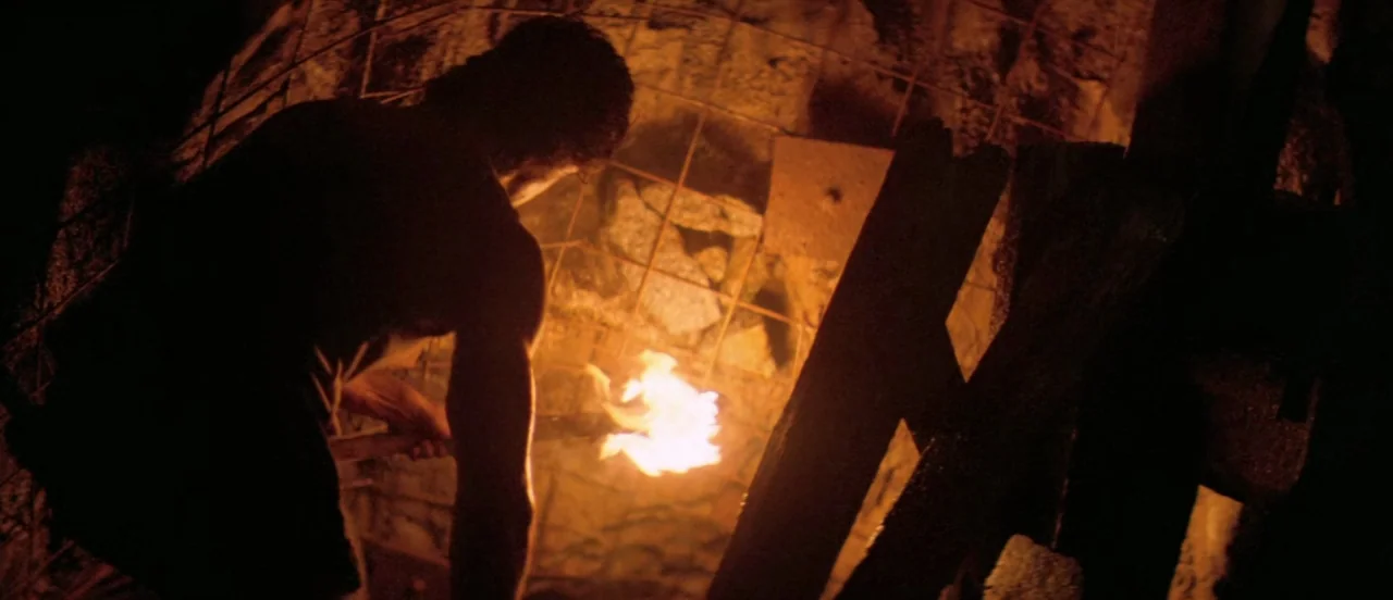 First Blood (1982) movie still: medium — A subterranean tunnel framed by jagged wooden supports and wire mesh walls. A man holds a flaming torch…