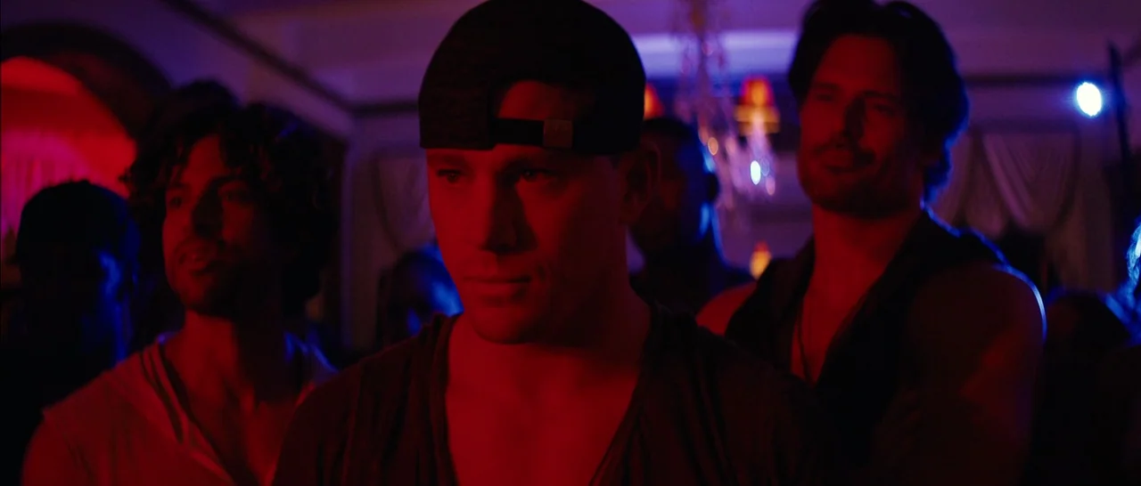 Magic Mike XXL (2015) movie still: medium — A dimly lit interior space with dark walls and curtains in the background. Three men stand together…