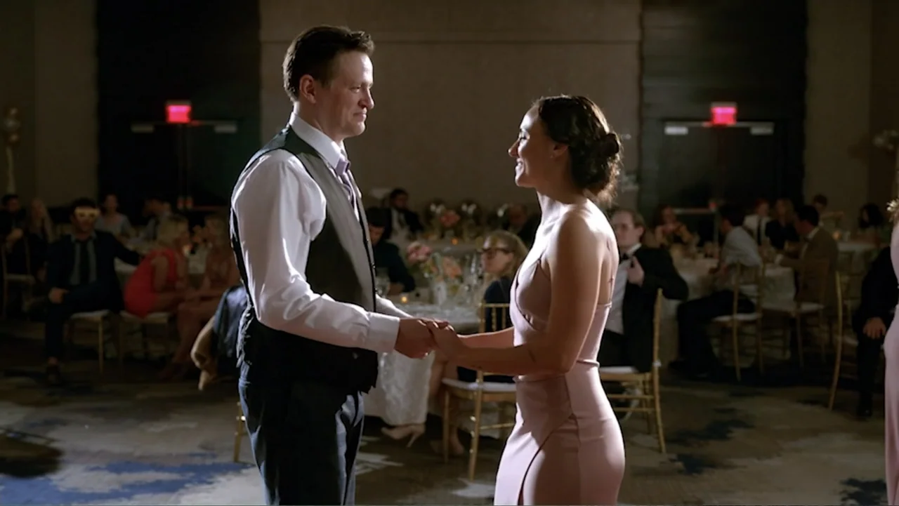 Ask Me to Dance (2022) movie still: fullbody — A spacious hotel ballroom with scattered dining tables and guests seated in the background. A man and…