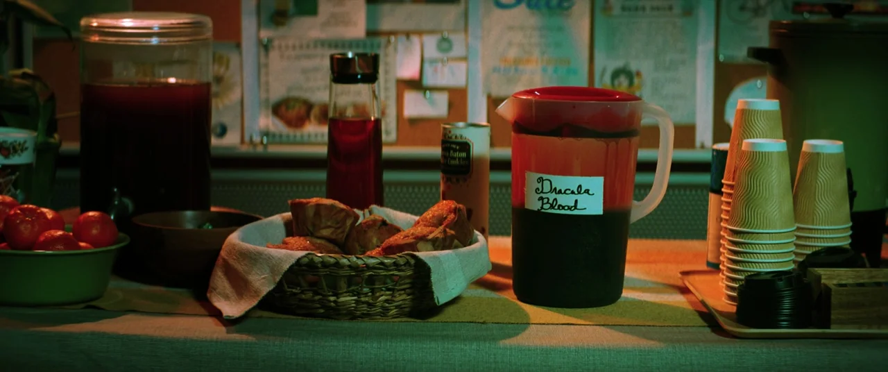 Renfield (2023) movie still: closeup — A refreshment table features a large pitcher labeled Dracula Blood with various snacks. A woven basket…