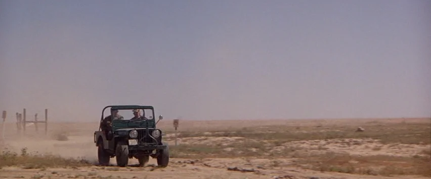 Scarecrow (1973) movie still: wide — A wide desert landscape with sparse vegetation and a dusty, unpaved trail. Two men ride in an open-top green…