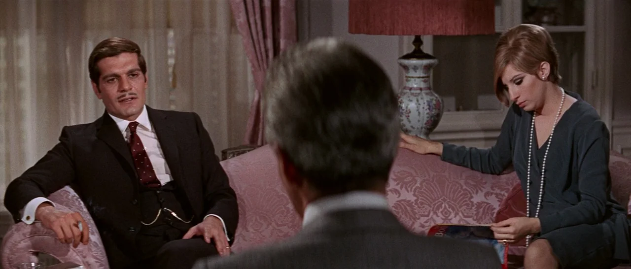 Funny Girl (1968) movie still: medium — An elegant 1960s interior features a tufted pink fabric sofa and patterned curtains. A man in a suit and a…