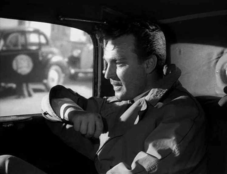 I Vitelloni (1953) movie still: medium — A man sits in the passenger seat of a mid-century car. He leans against the door while looking through the…