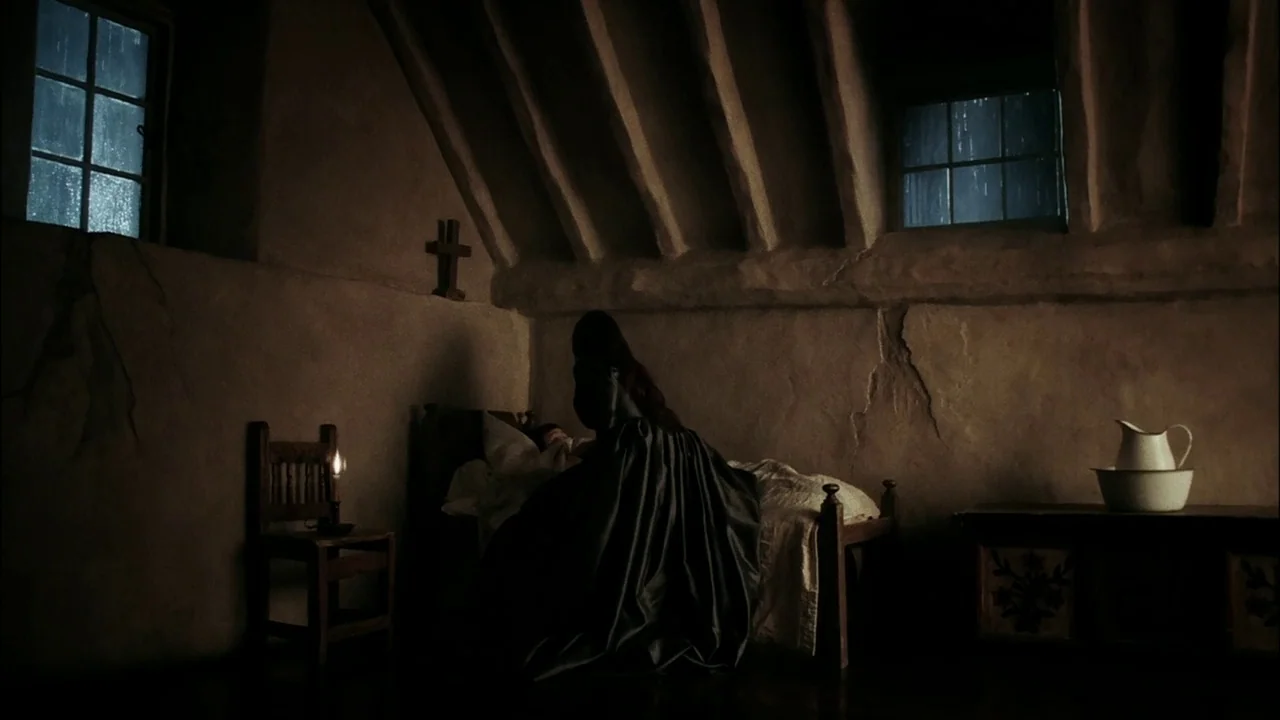 Sleepy Hollow (1999) movie still: medium — An attic bedroom with a sloped wooden beamed ceiling and rough stone walls. A person in a black cloak…
