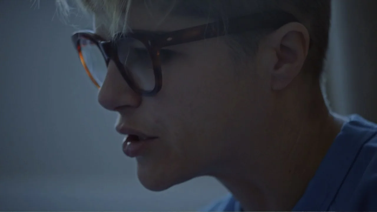 Introducing, Selma Blair (2021) movie still: closeup — A close-up view of a person indoors in a dimly lit, nondescript room. The person in…