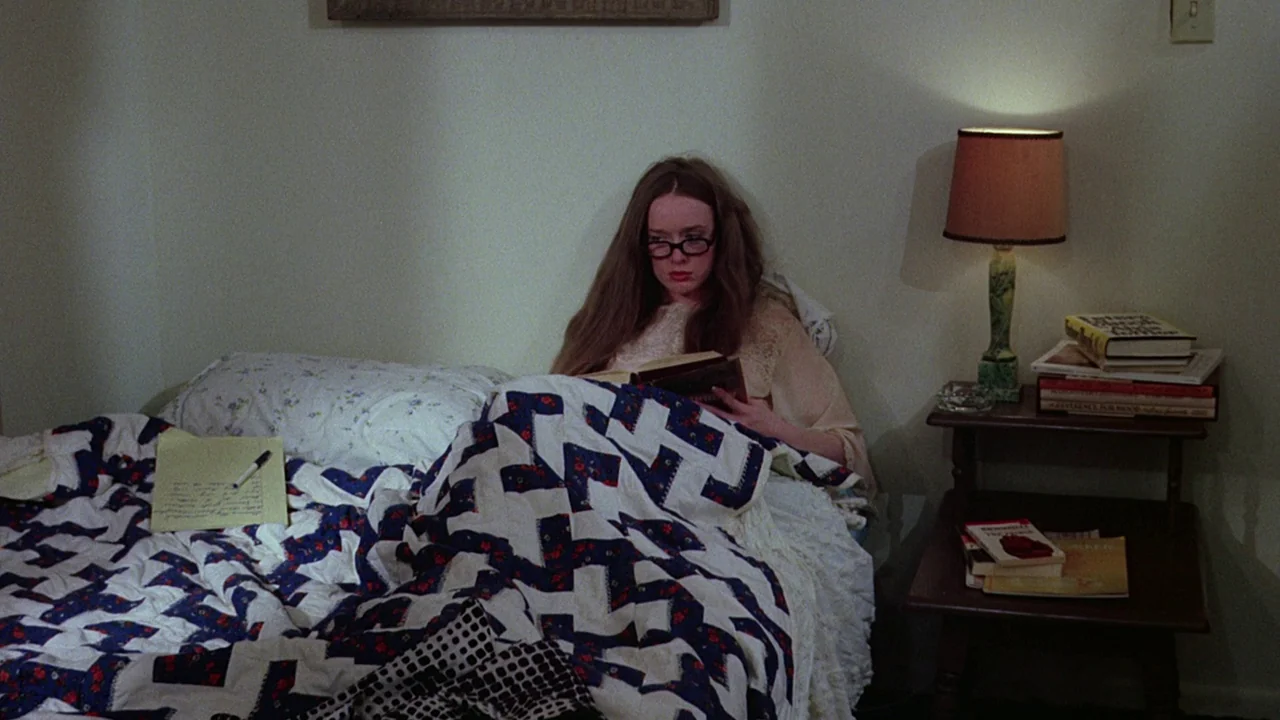 I Spit On Your Grave (1978) movie still: medium — A woman sits propped up in a bed covered by a patterned quilt. Beside her is a wooden side table…