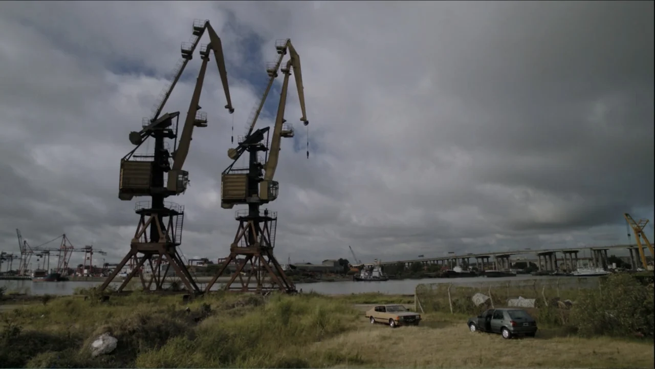 A Boyfriend for My Wife (2008) movie still: wide — A desolate industrial waterfront features two massive yellow cranes towering over a muddy river.…