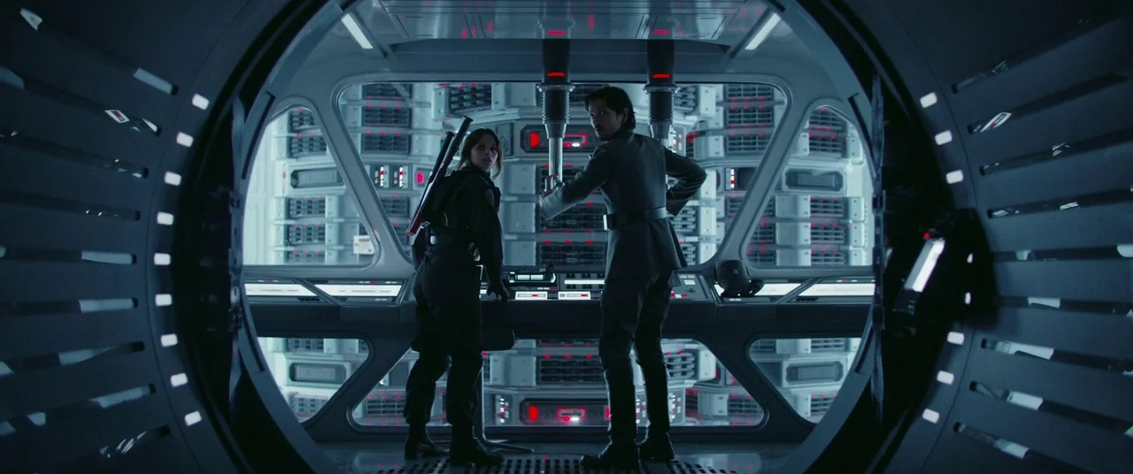 Rogue One: A Star Wars Story (2016) movie still: wide — A high-tech data storage facility features rows of illuminated server banks behind a…