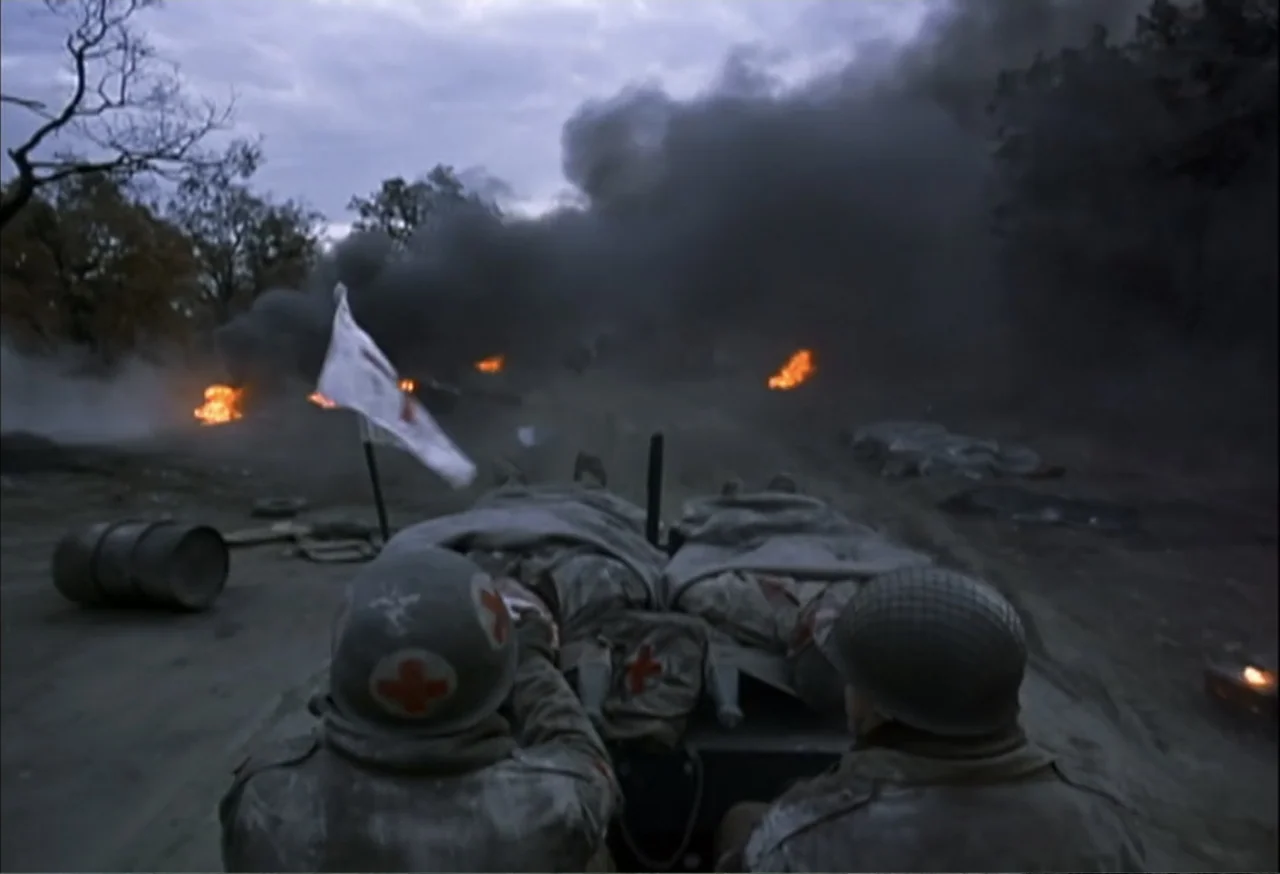When Trumpets Fade (1998) movie still: medium — A war-torn field with thick dark smoke, scattered fires, and mud-covered terrain. Two soldiers in…