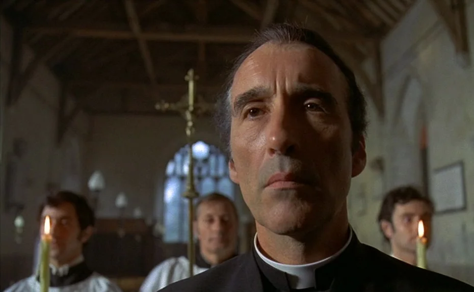 To The Devil a Daughter (1976) movie still: closeup — A stone interior with arched windows and exposed wooden rafters suggests a church setting. A…