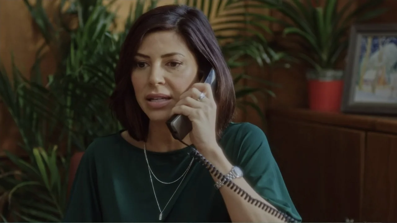A Christmas Break (2020) movie still: medium — An office interior features indoor plants and wood paneled cabinetry in the background. A woman in a…