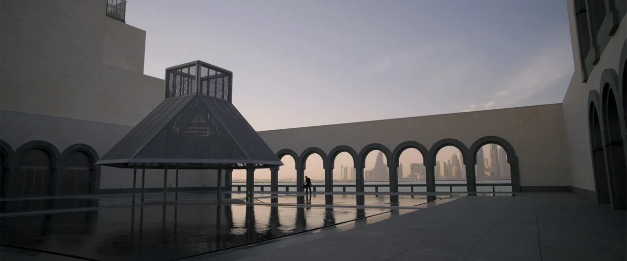 Operation Fortune: Ruse de Guerre (2023) movie still: wide — A modern stone courtyard features a glass pyramid structure and an arched colonnade…