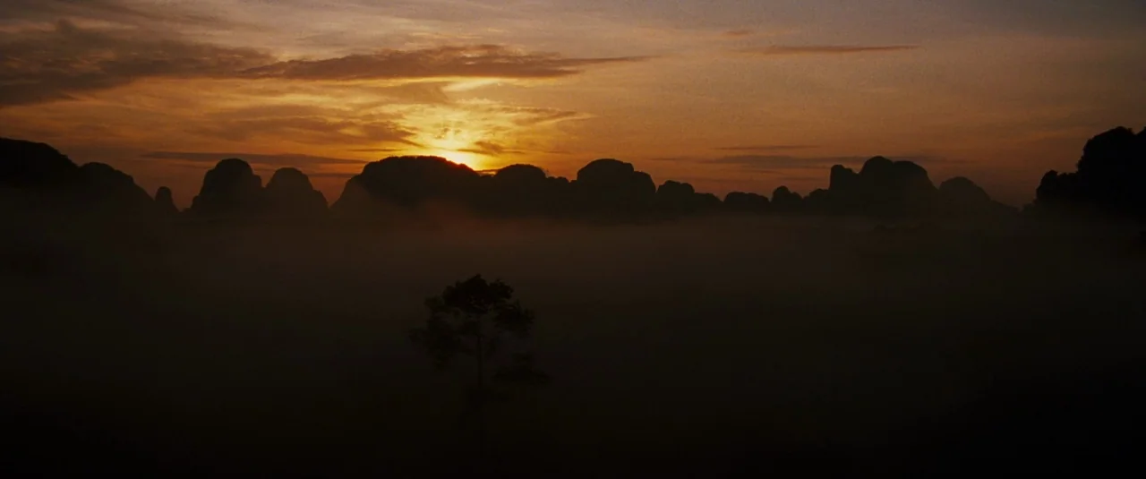 The Hangover Part II (2011) movie still: establishing — A dark valley floor is blanketed in thick fog during a sunset. Jagged mountain silhouettes…