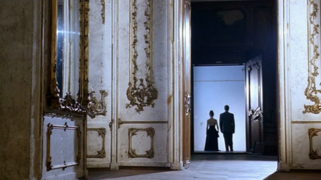Malina (1991) movie still: wide — An opulent room with white marble walls and intricate gold-leaf rococo carvings. A man and a woman stand together…