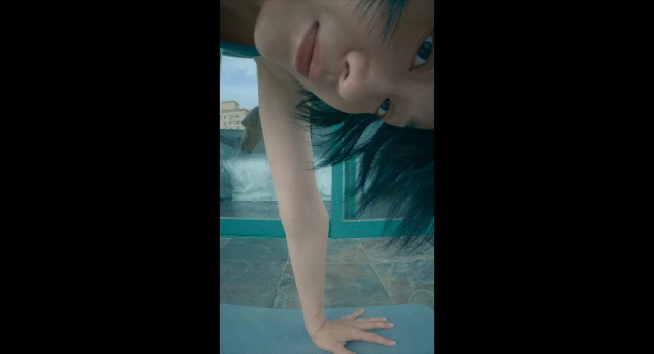 White River (2023) movie still: closeup — A person leans toward the camera from an elevated balcony with a view. The frame is rotated vertically,…