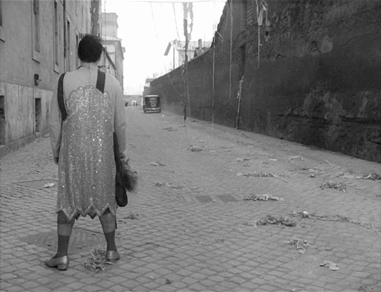 I Vitelloni (1953) movie still: fullbody — A desolate, narrow cobblestone road stretches between high, weathered stone walls. A lone person in a…