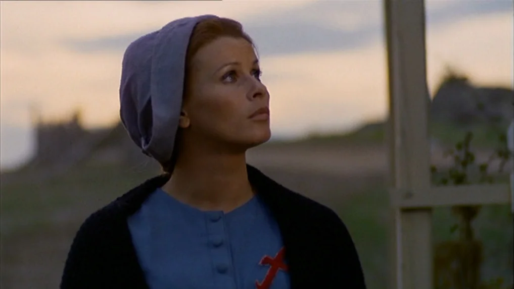 The Scarlet Letter (1973) movie still: medium — An open landscape with a sunset sky serves as the backdrop. A young woman with a head covering gazes…