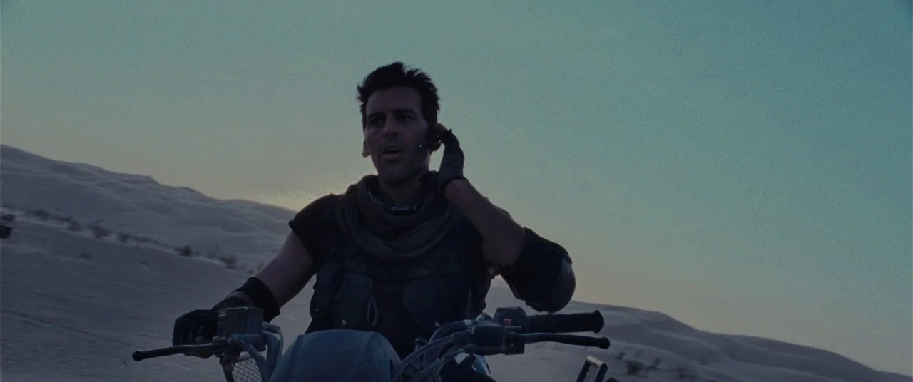 Resident Evil: Extinction (2007) movie still: medium — A man rides across vast sand dunes at dusk with a clear horizon. He holds a small device to…