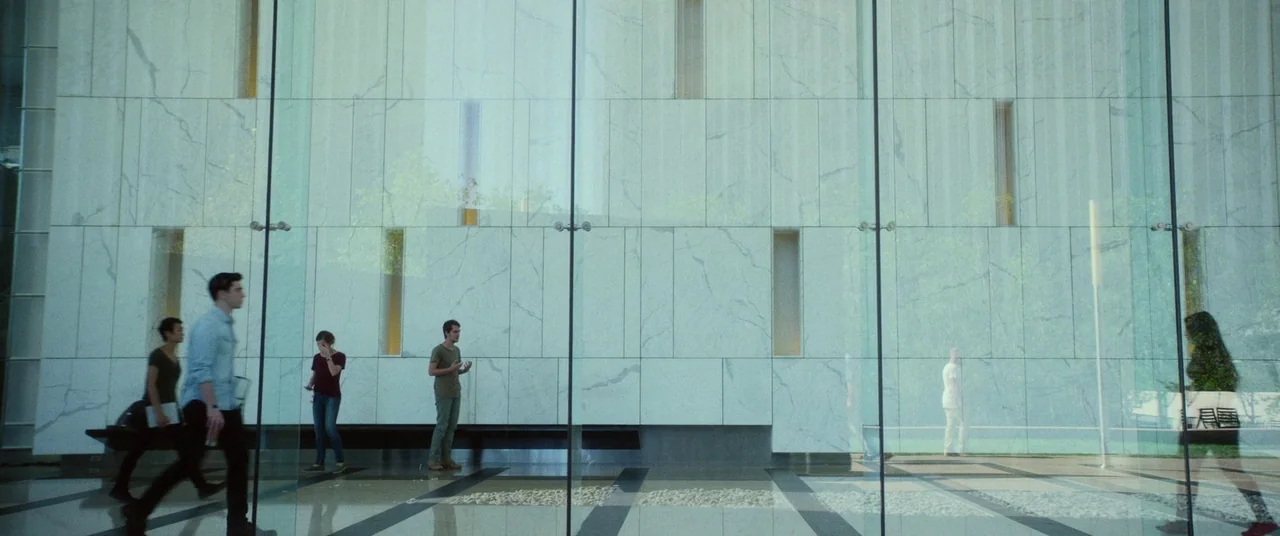 The Circle (2017) movie still: wide — A spacious lobby features floor-to-ceiling glass windows and white marble wall panels. Multiple individuals…