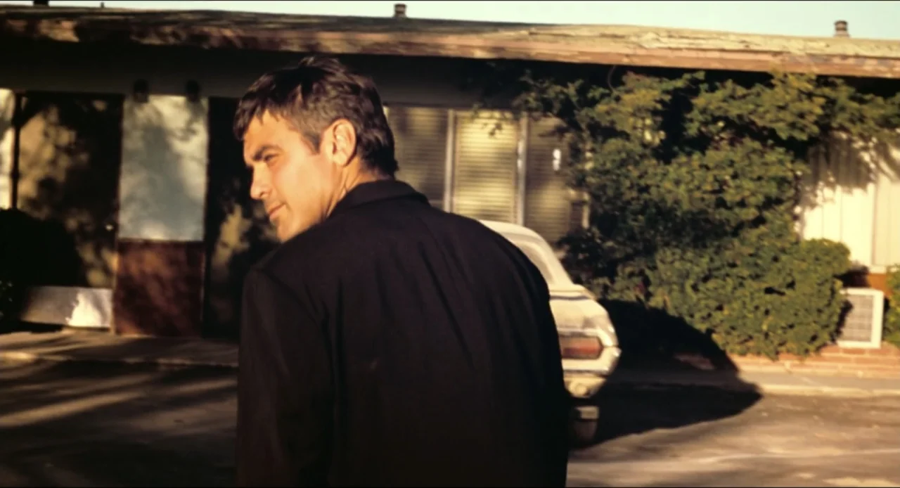 From Dusk Till Dawn (1996) movie still: medium — A single-story motel building stands under late afternoon light in a paved lot. A man wearing a…