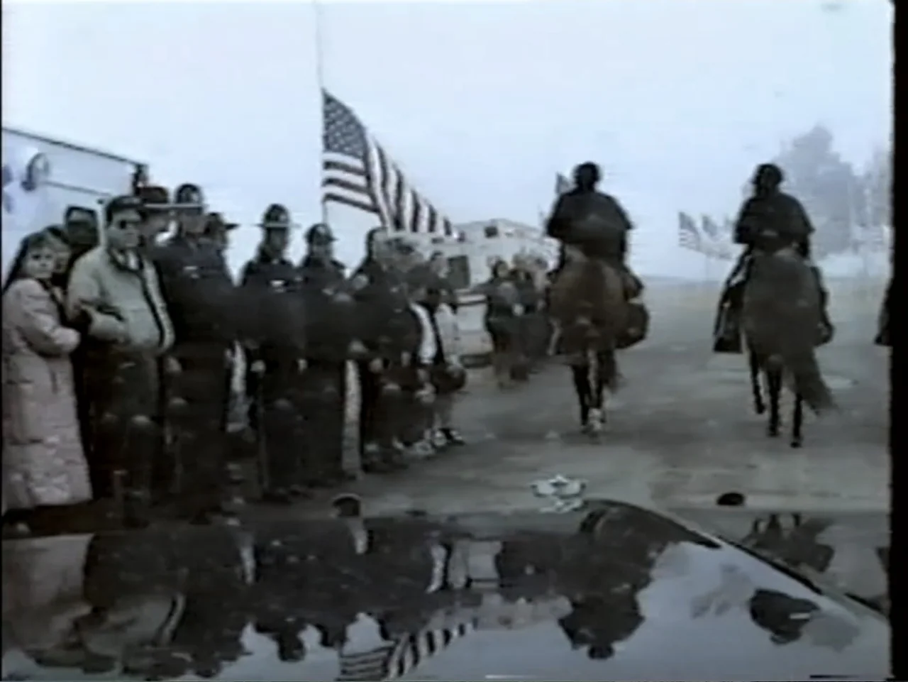 5 American Handguns - 5 American Kids (1995) movie still: wide — A group of police officers and civilians stand on an asphalt lot in fog. Two…