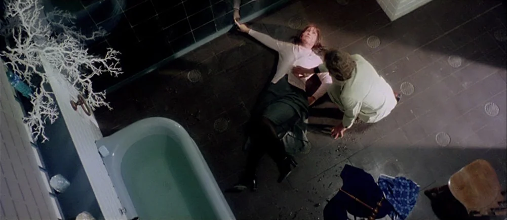 Deep Red (1975) movie still: wide — A spacious tiled bathroom contains a bathtub and an ornamental white skeletal sculpture structure. A man kneels…