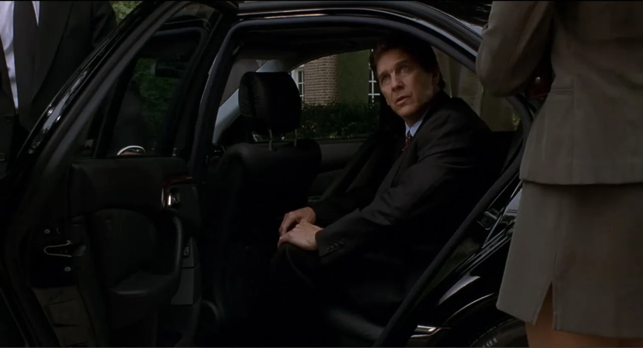 National Lampoon's Van Wilder (2002) movie still: medium — A man sits in the back of a black luxury car during the day. A woman in a grey suit…