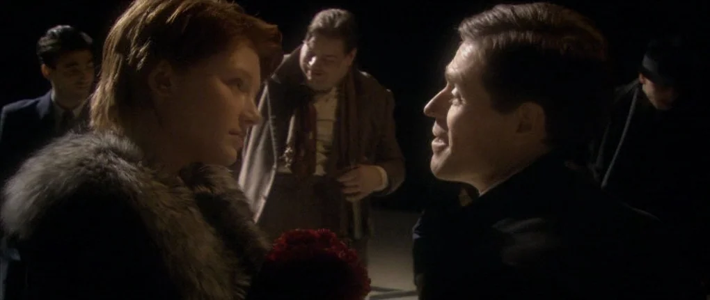 Manderlay (2005) movie still: medium — People gather in a dark, indistinct outdoor space at night. A woman in a fur-collared coat talks to a man…