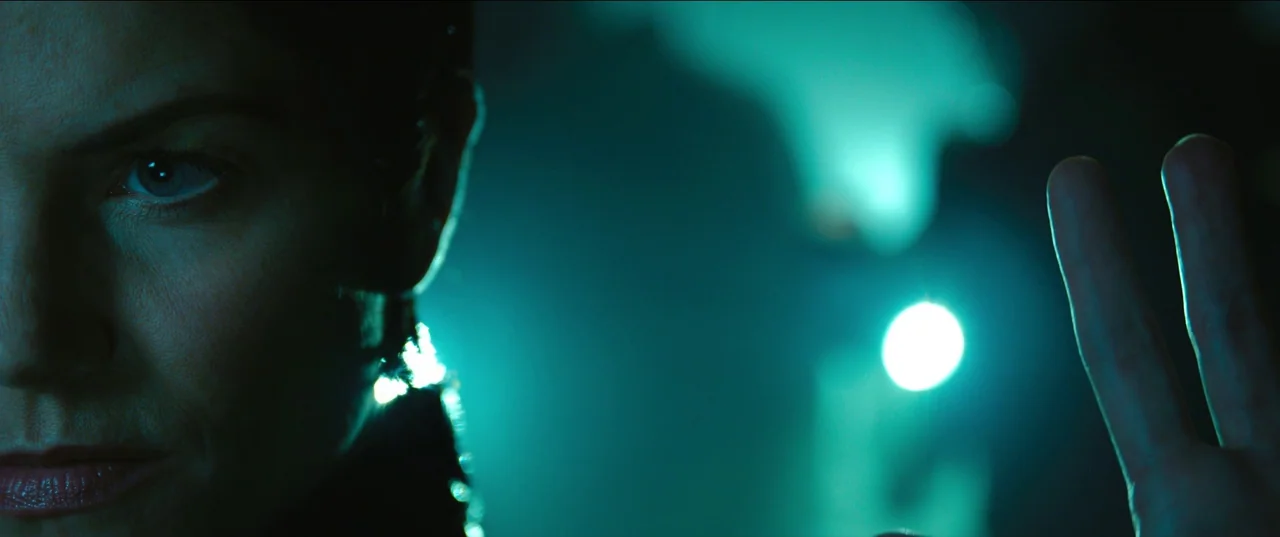 The Matrix Resurrections (2021) movie still: closeup — A dark space lit by a singular, bright teal light in the background. A woman's face in…