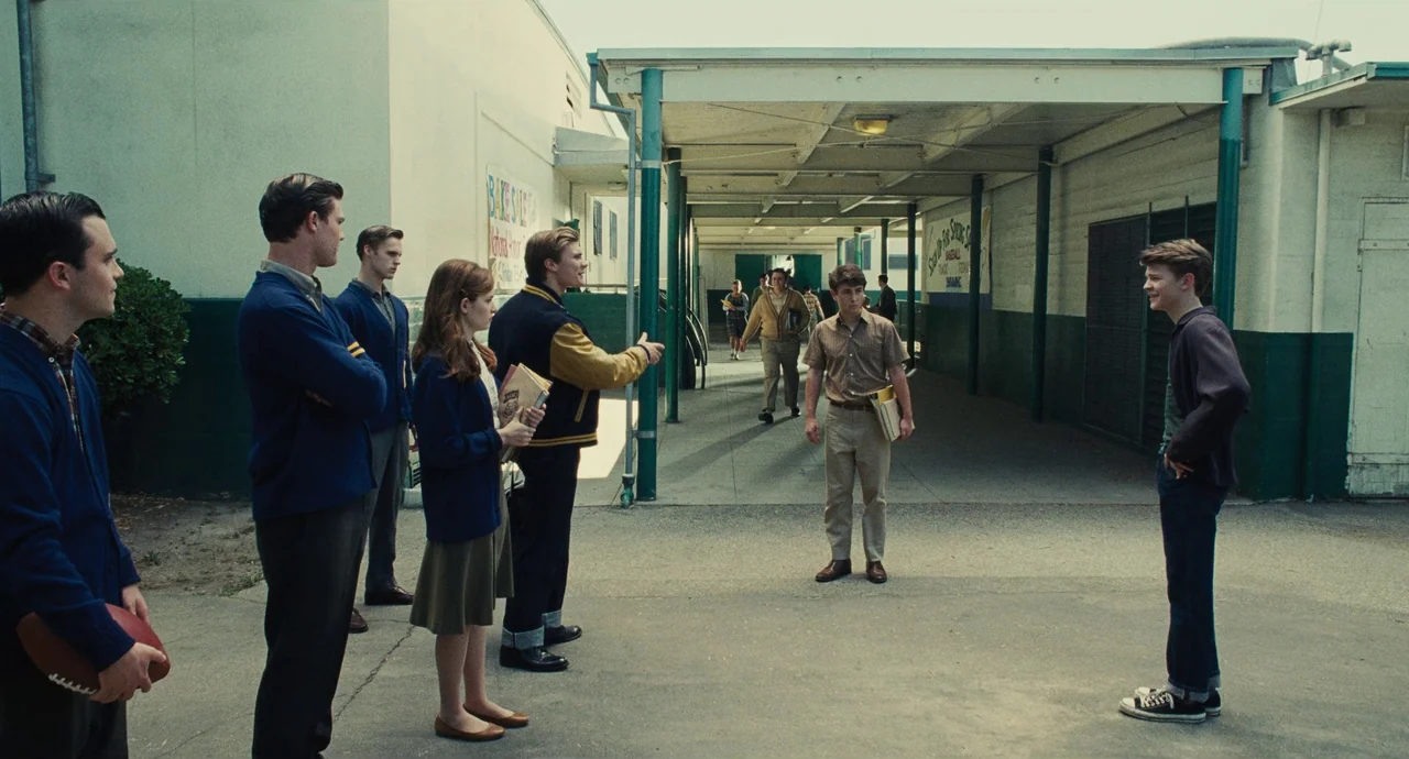 The Fabelmans (2022) movie still: wide — An outdoor school corridor with covered walkways and painted green trim on the buildings. A group of…