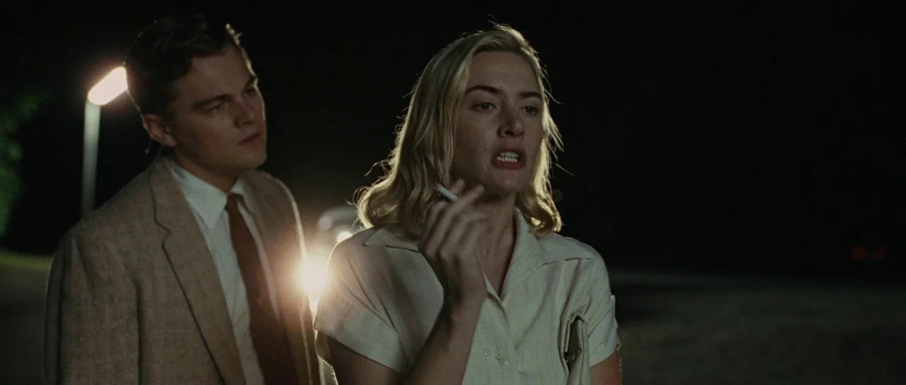 Revolutionary Road (2008) movie still: medium — A dark outdoor setting at night features two people illuminated by distant artificial light. The…