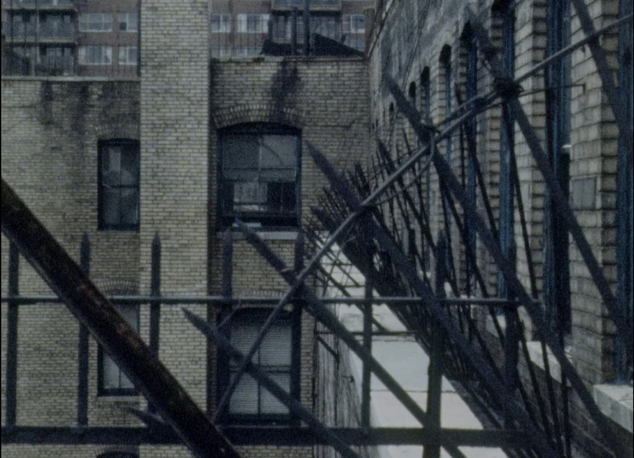 Hotel Monterey (1973) movie still: establishing — An exterior view of a tall, grimy city building features weathered yellow brick walls. A black…