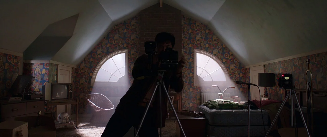 The Conjuring 2 (2016) movie still: medium — An attic room features slanted ceilings, patterned wallpaper, and two arched windows. A man stands…